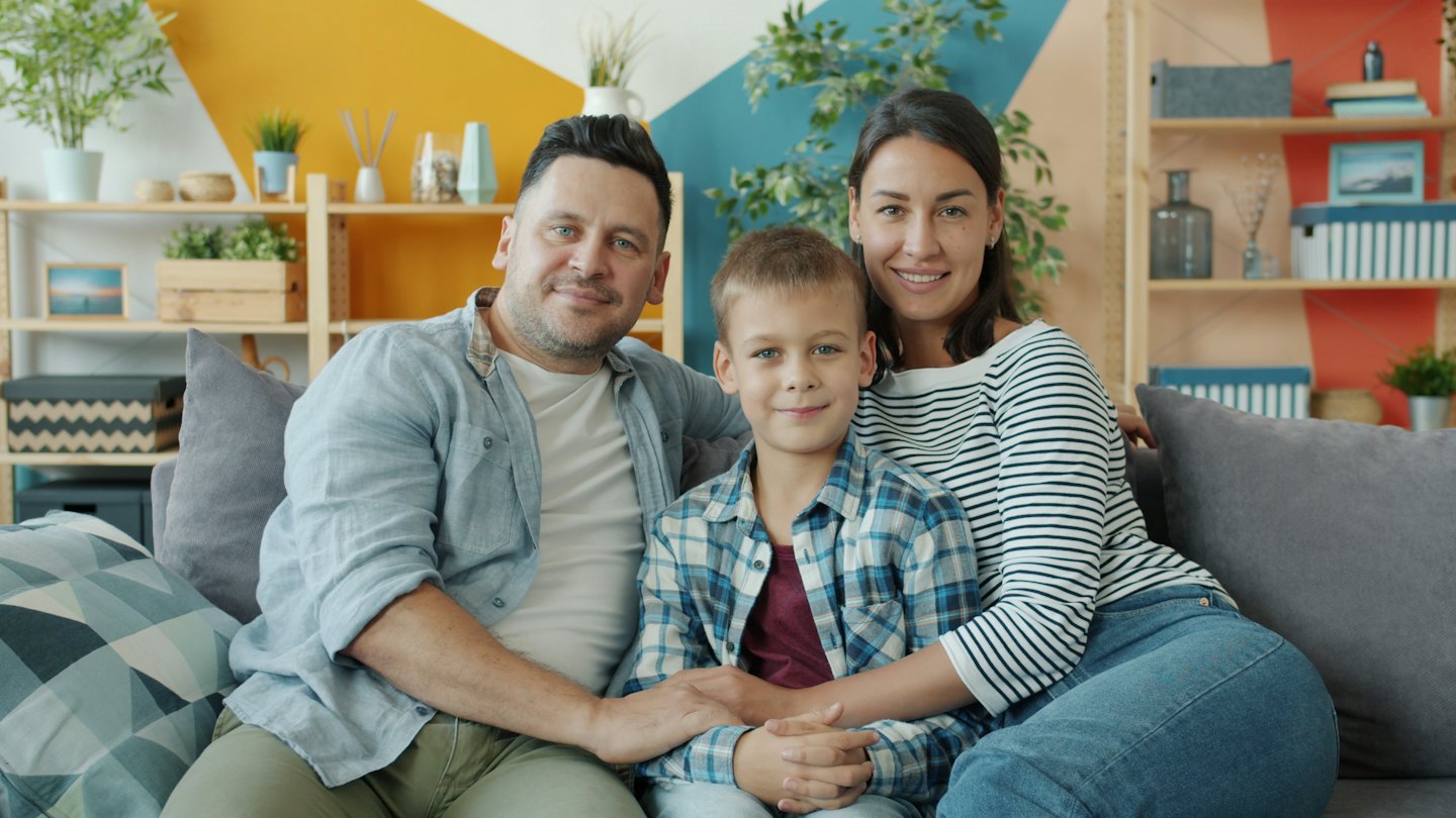 Famille souriante sur un canapé gris dans un salon moderne.