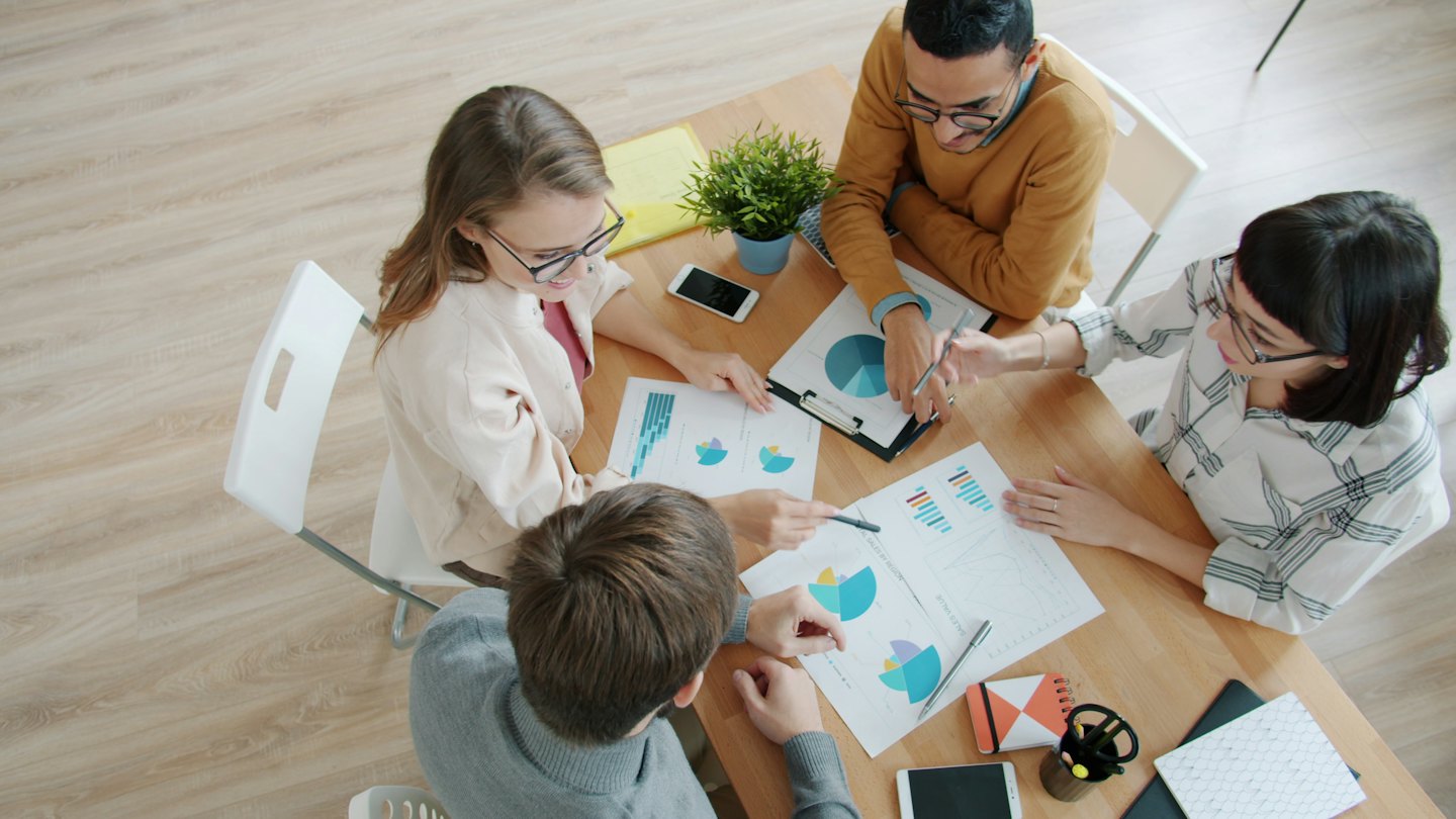 Une équipe d'affaires diversifiée collabore autour de tableaux financiers à une table.