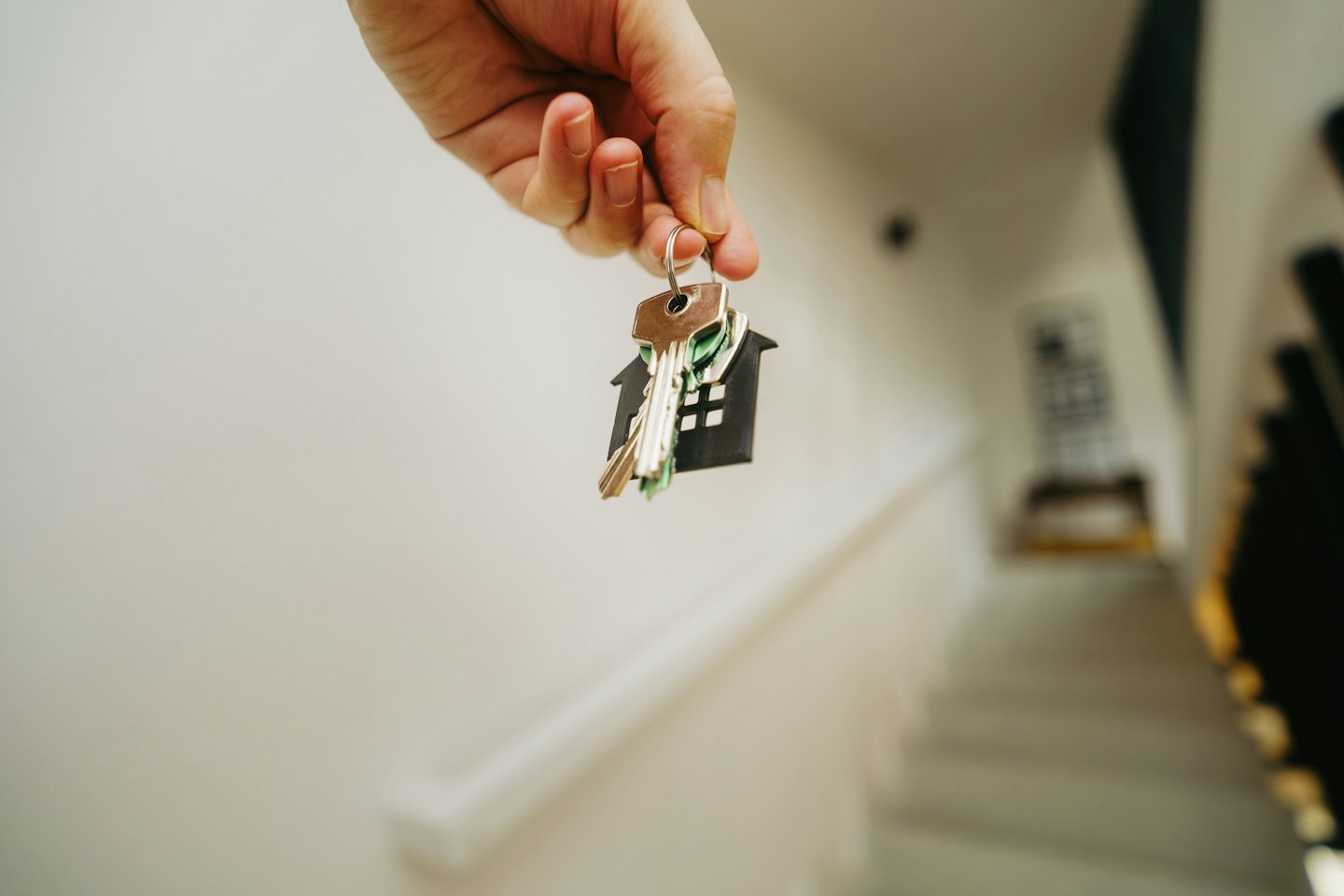 Une main tenant des clés de maison avec un porte-clés en forme de maison.
