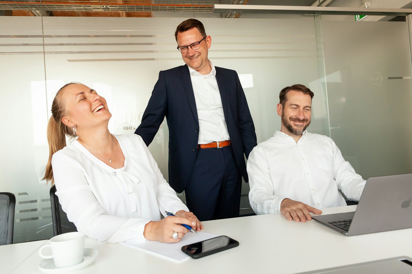 Trois professionnels souriants collaborent autour d'une table dans un bureau moderne.