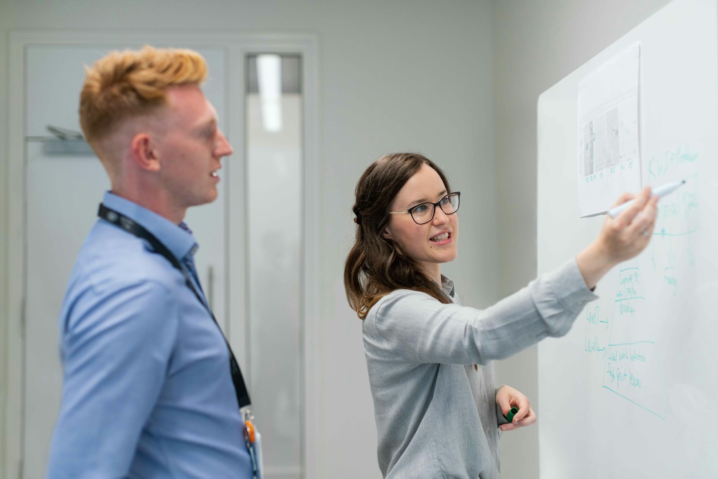 Deux professionnels collaborant sur un tableau blanc dans un bureau moderne.