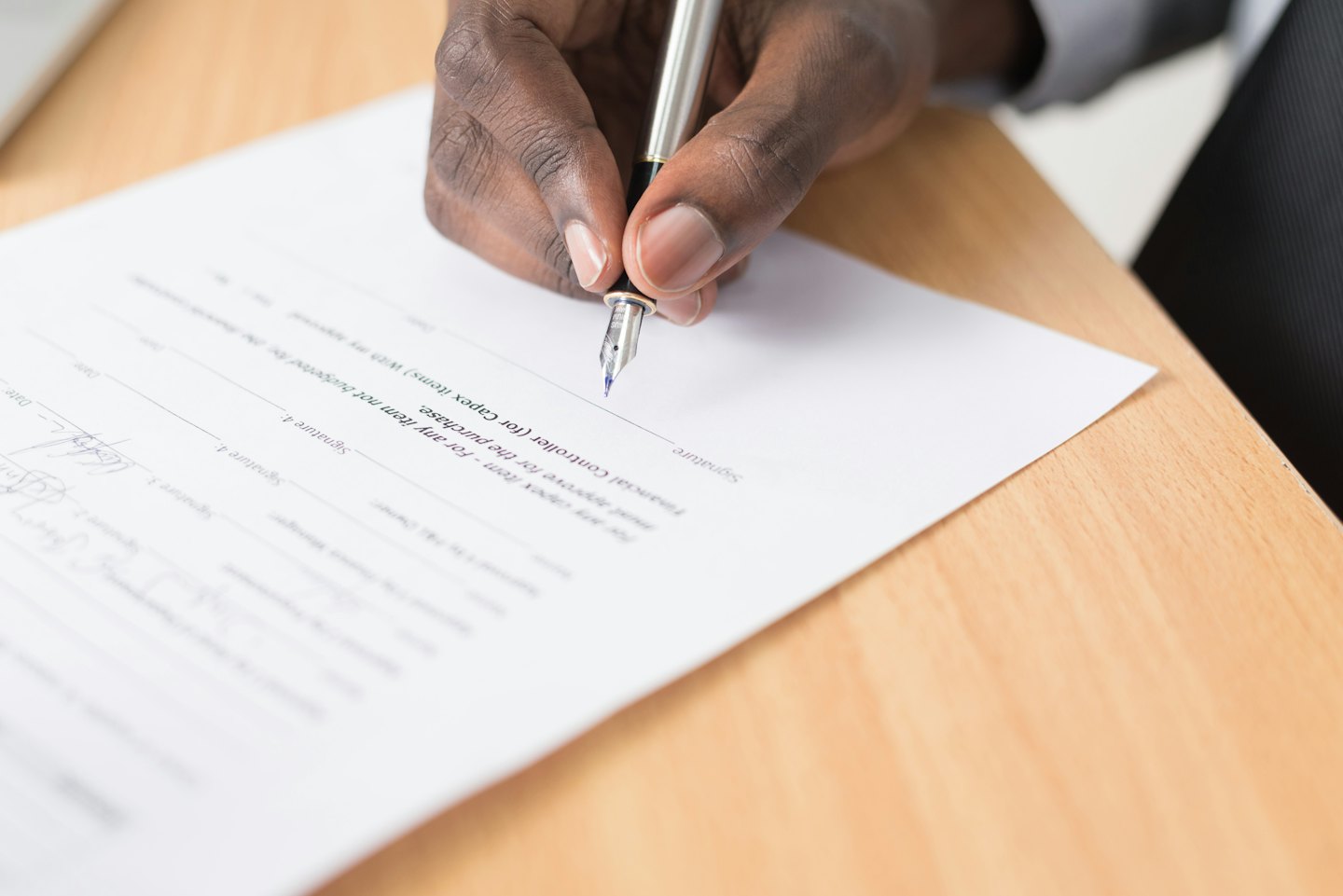 Une main signant un document avec un stylo plume à un bureau.