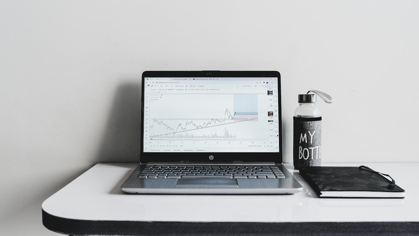 Ordinateur portable avec des graphiques financiers à côté d'un carnet et d'une bouteille d'eau.