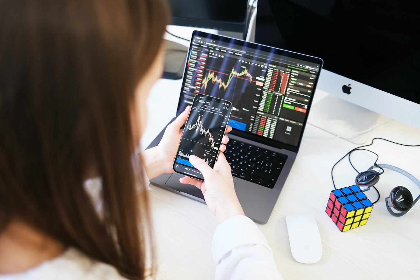 Une personne fait du trading d'actions sur son téléphone et son ordinateur portable dans un bureau.
